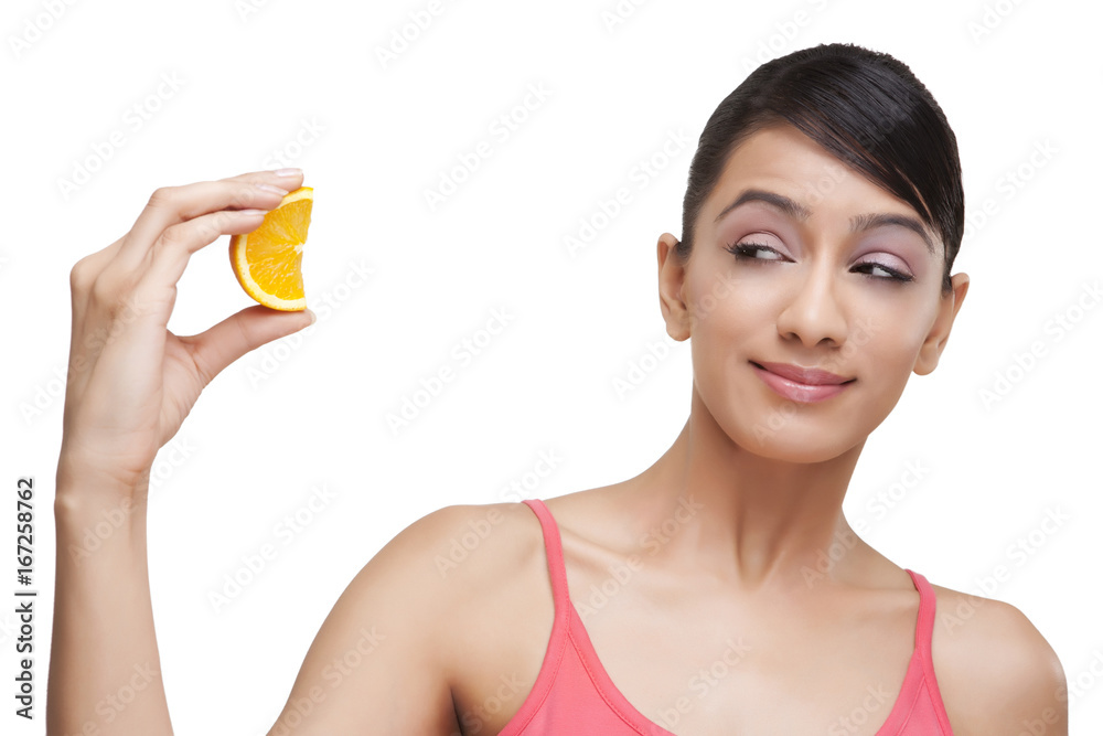 Close-up of woman squeezing orange slice while looking over white background Close-up of woman squeezing orange slice while looking over white background