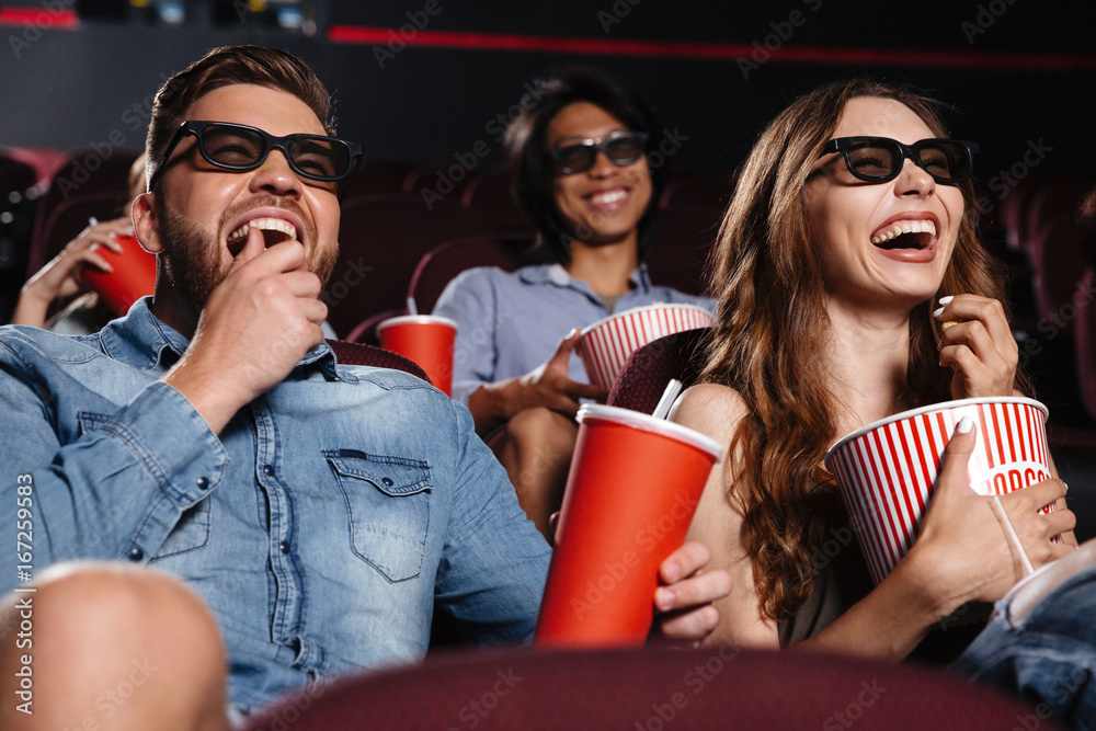 Naklejka premium Śmiejący się przyjaciele siedzący w kinie oglądają film