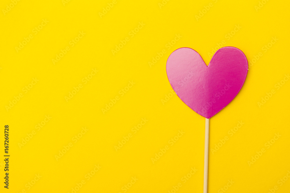 Paper heart on a stick over a bright yellow background