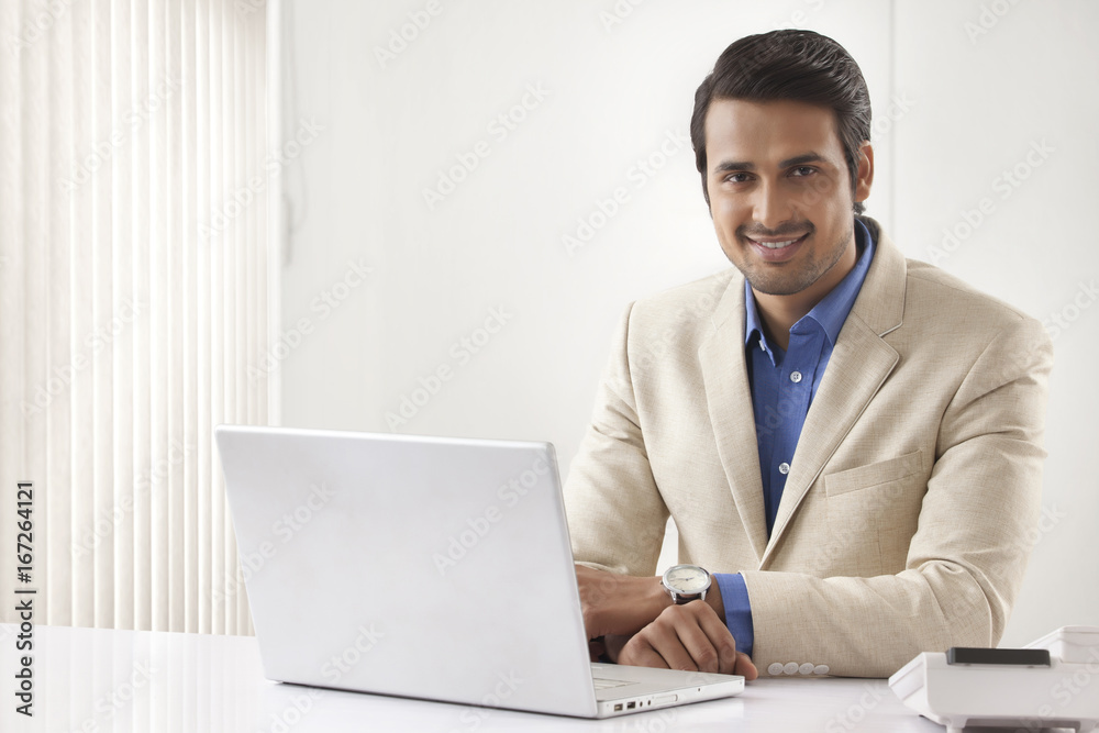 Portrait of happy Indian businessman with laptop sitting at office desk Portrait of happy Indian businessman with laptop sitting at office desk