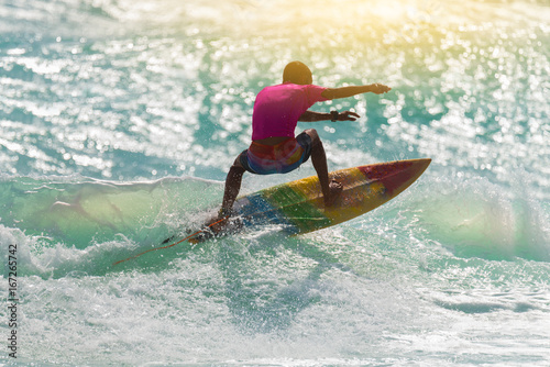Obraz Sylwetka surfing o zachodzie słońca. Szczęśliwy surfer cieszy się dużą falą podczas wakacji na tropikalnej wyspie.