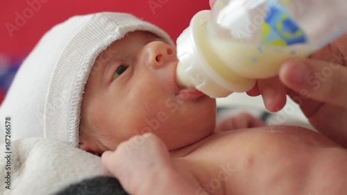 A newborn baby boy eats a nutritious mixture or milk from a bottle with a pacifier
