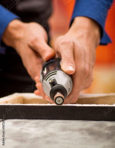 Closeup of a hardworker man using a polisher in a wooden frame, in selective focus on a gray table in a blurred background