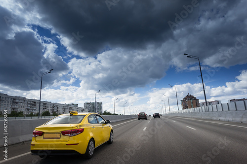 A cab at high speed on a motorway in an urban area with the lit taxi sign on top of its roof