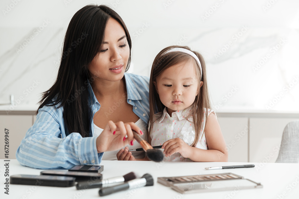 Woman with little daughter at home indoors doing makeup. Woman with little daughter at home indoors doing makeup.