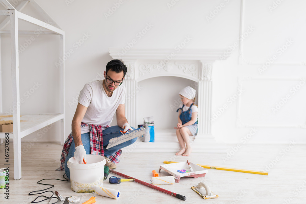 The young serious man does repair at home, his daughter sits behind him The young serious man does repair at home, his daughter sits behind him