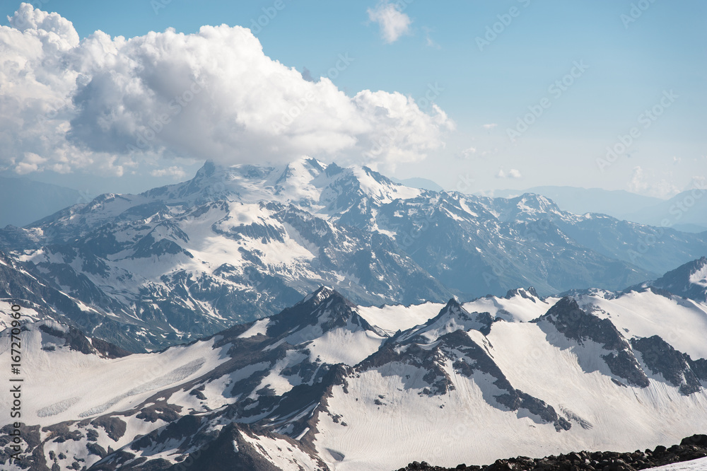 Naklejka premium Dark blue sky with clouds on the rocky peaks of the mountains covered with glaciers and snow