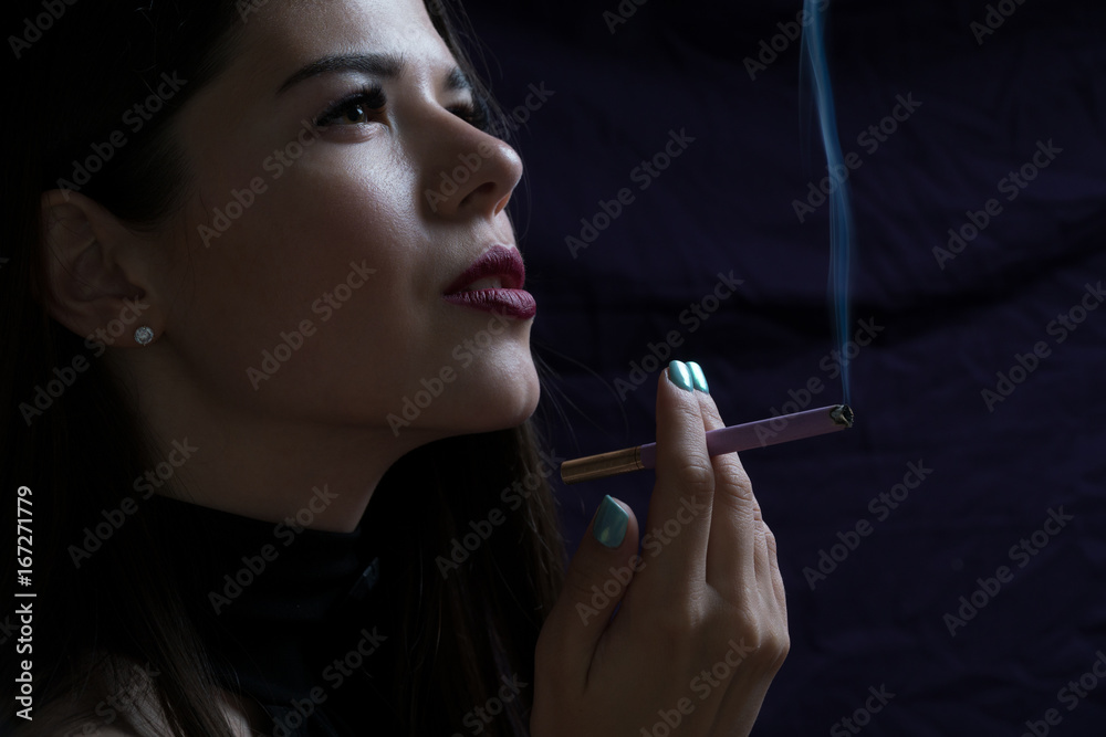 Obraz premium Portrait of the beautiful elegant girl smoking cigarette isolated on dark background