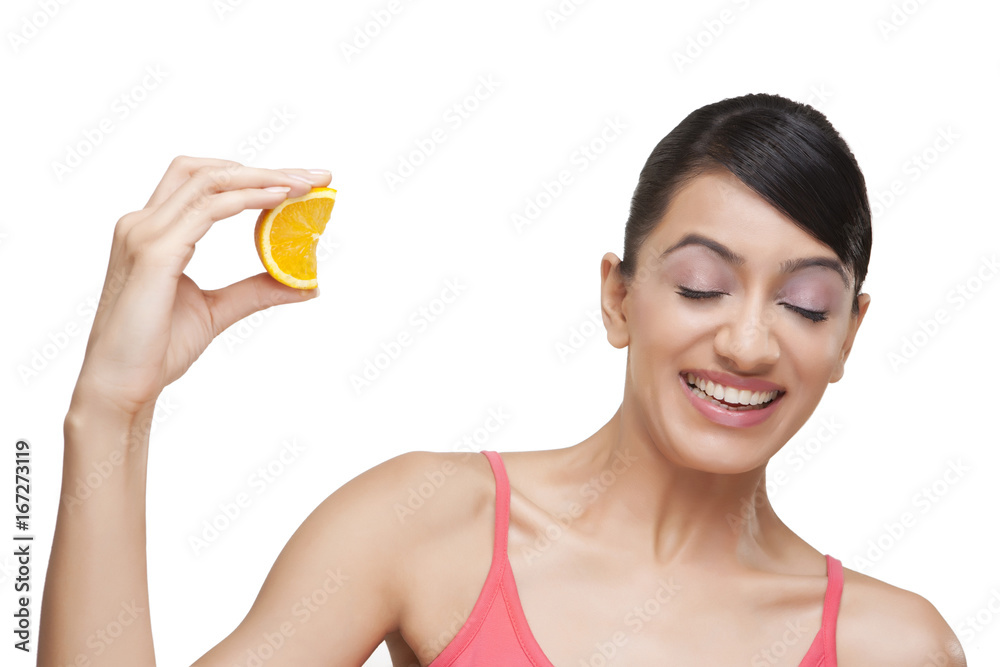 Close-up of woman squeezing orange slice while making face over white background Close-up of woman squeezing orange slice while making face over white background