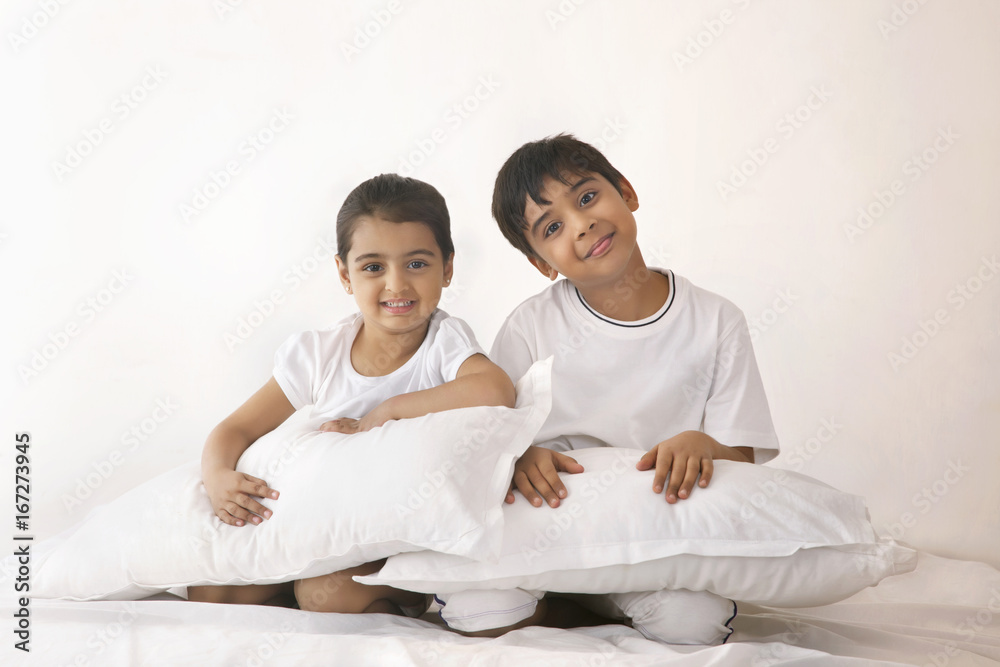 Portrait of happy siblings with pillows sitting in bed Portrait of happy siblings with pillows sitting in bed