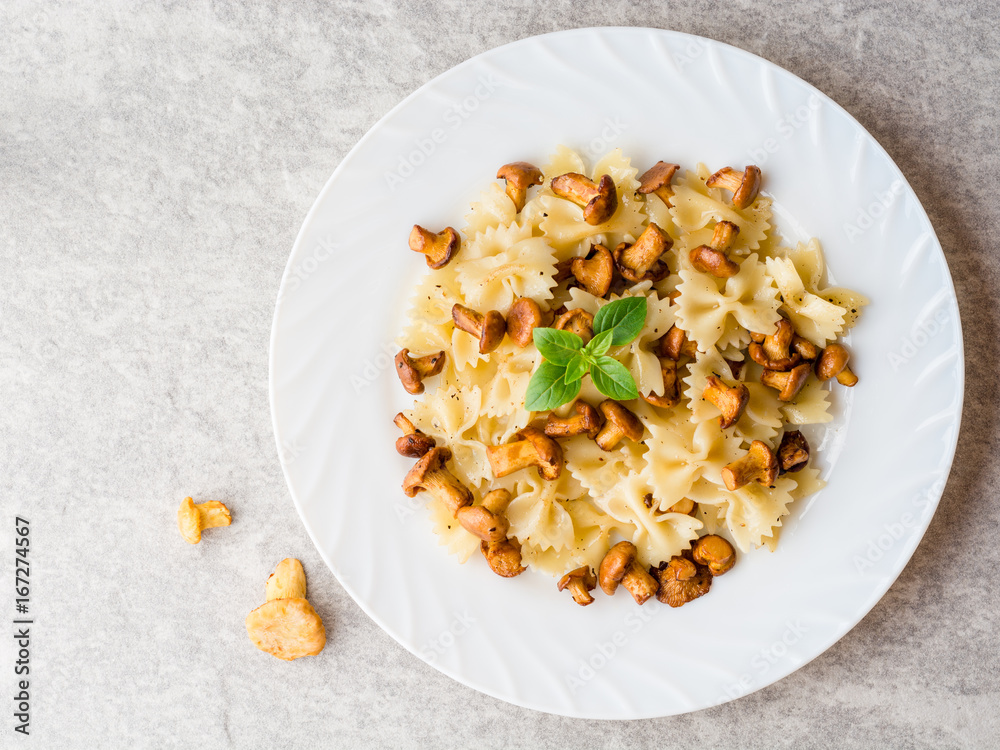Farfalle pasta with chanterelles and basil on gray stone background