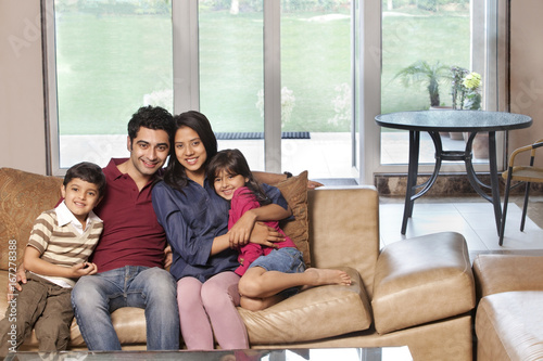 Portrait of happy young parents sitting with children on sofa at home 