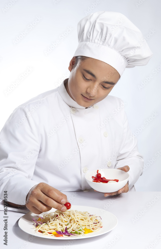 Chef placing cherry tomato on plate of noodles Chef placing cherry tomato on plate of noodles