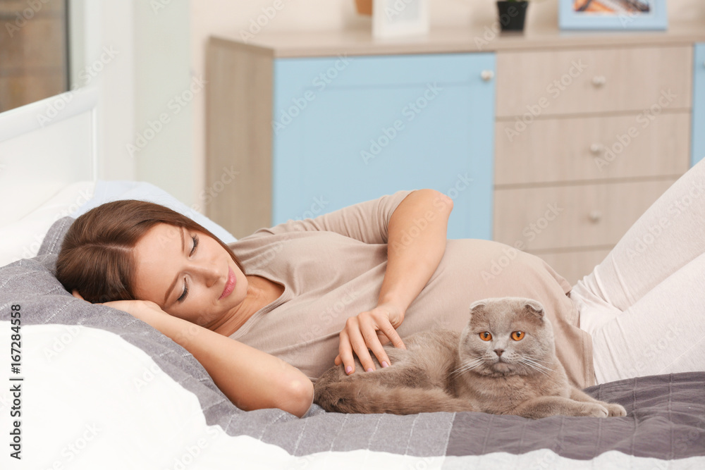 Young pregnant woman with cute cat lying on bed Young pregnant woman with cute cat lying on bed