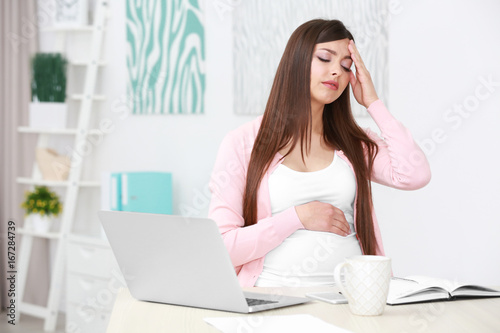 Beautiful young pregnant woman suffering from headache while working with laptop at home © Africa Studio