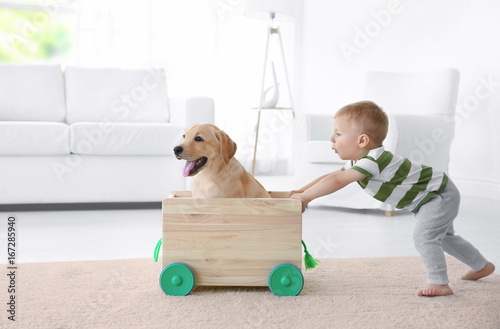 Cute child and Labrador Retriever playing with wooden toy cart at home