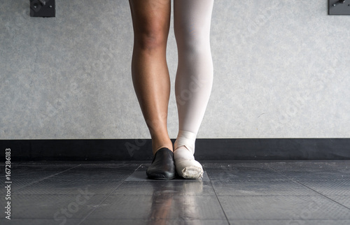 Dancer standing in parallel position at the barre, half dressed in Jazz dance attire and half in ballet attire