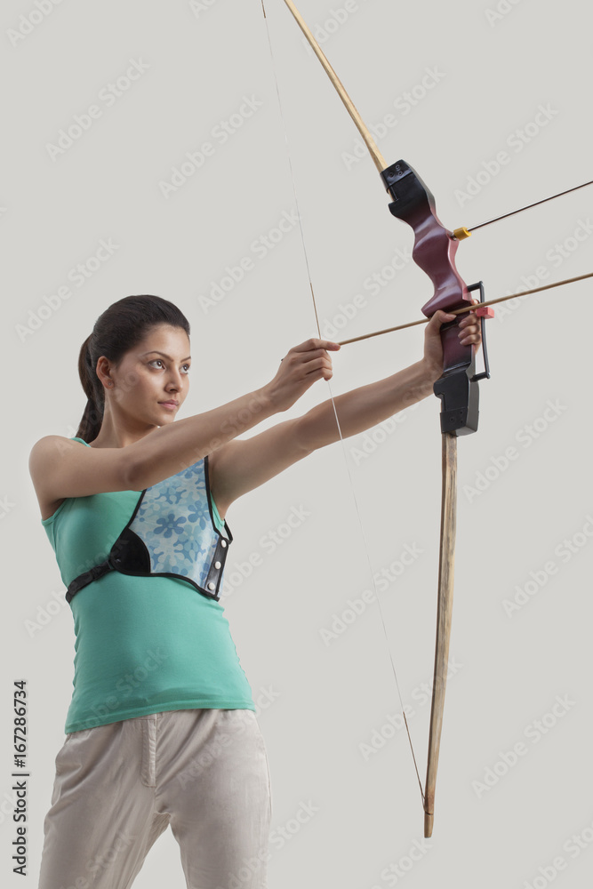 Woman practicing archery isolated over gray background Woman practicing archery isolated over gray background