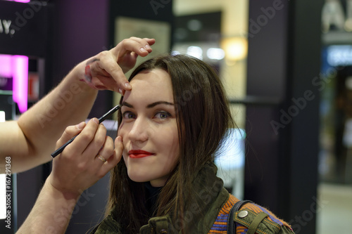 Beautiful brunette with red lipstick is testing the eyeshadows in beauty store