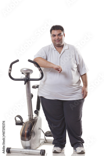 Full length of an obese man standing by an exercise bike over white background 