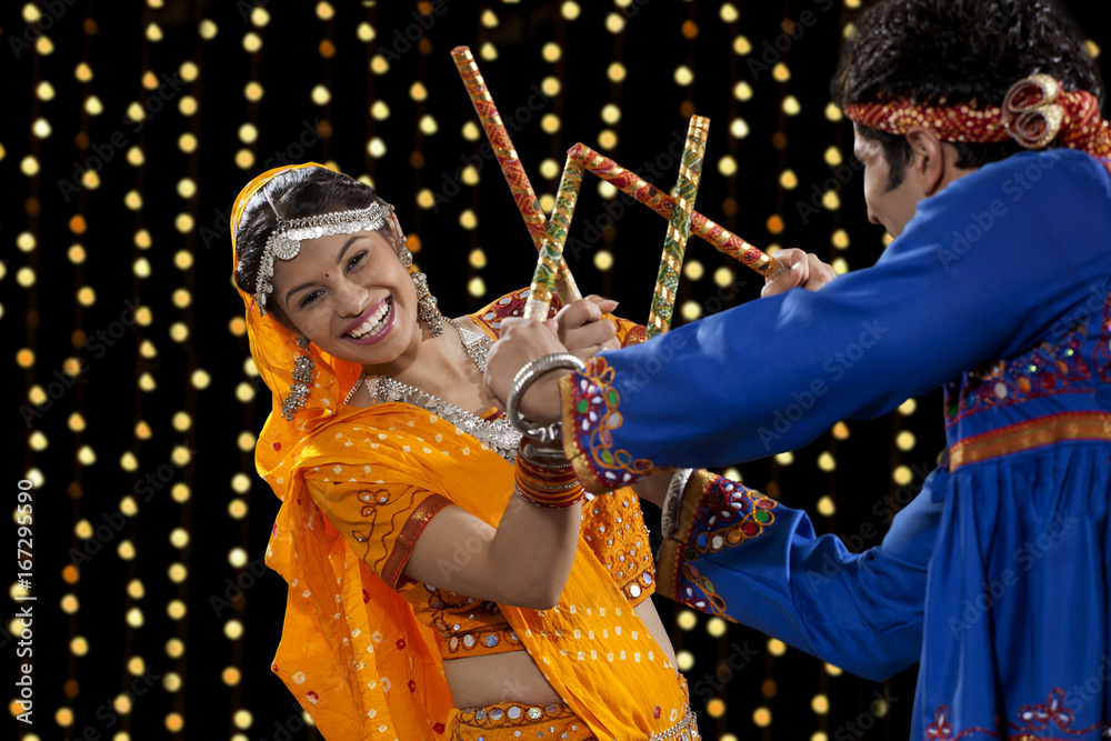 Portrait of happy young woman performing Dandiya Raas with man against neon lights