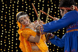 Portrait of happy young woman performing Dandiya Raas with man against neon lights