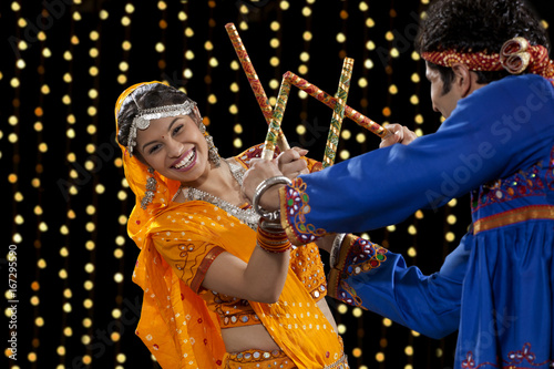 Portrait of happy young woman performing Dandiya Raas with man against neon lights