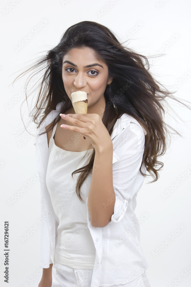 Portrait of beautiful young woman eating ice cream cone over white background