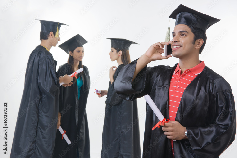 Happy graduate student answering smart phone with friends discussing against white background Happy graduate student answering smart phone with friends discussing against white background