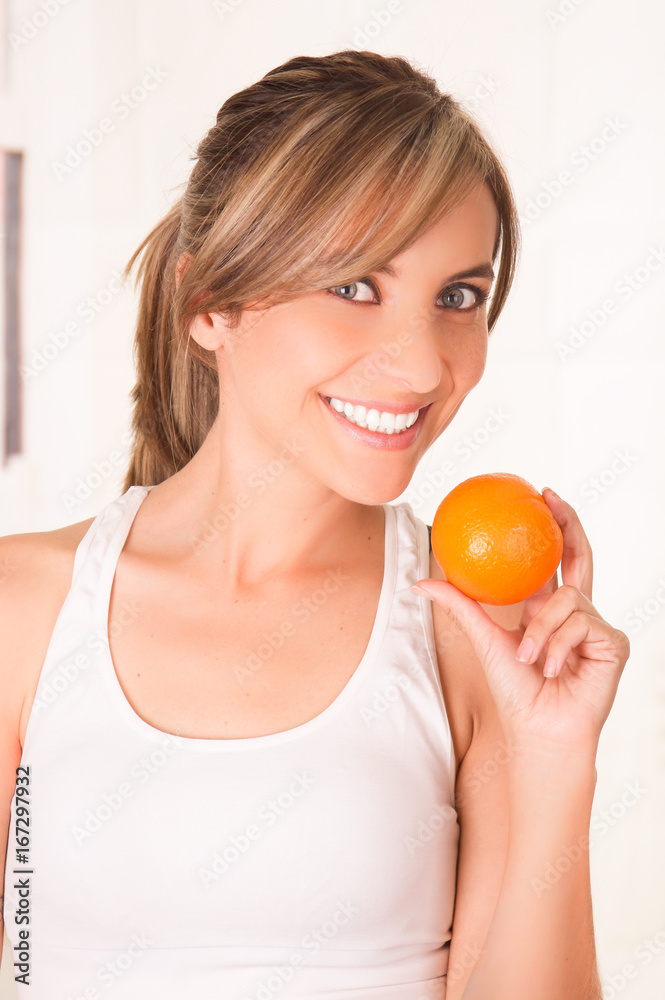 Beautiful young smiling woman wearing a white t-shirt and holding a healthy orange Beautiful young smiling woman wearing a white t-shirt and holding a healthy orange