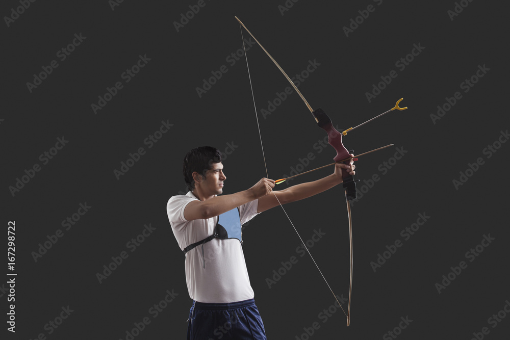 Obraz premium Male archer aiming against black background