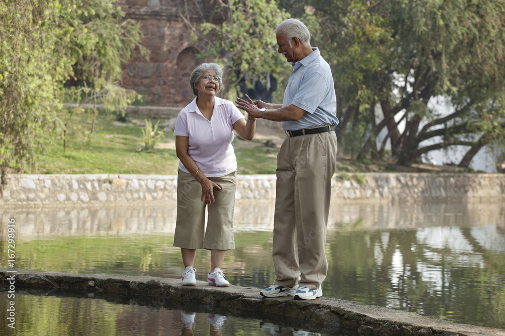 Mature woman afraid of walking on narrow bridge with man at park 