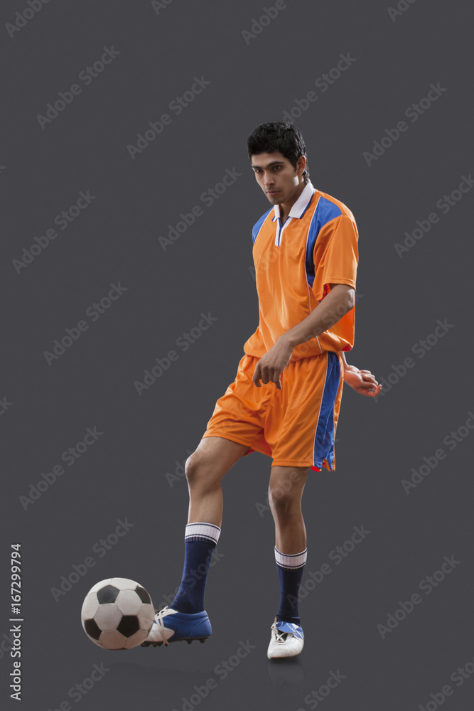 Young Indian male player playing soccer isolated over gray background