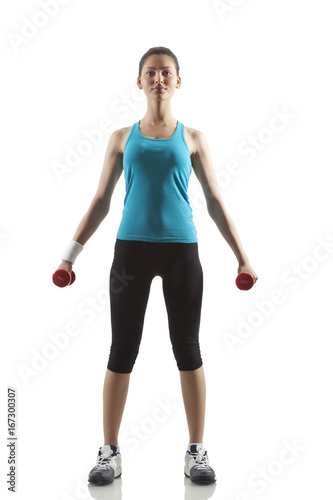 Portrait of young woman lifting dumbbells against white background