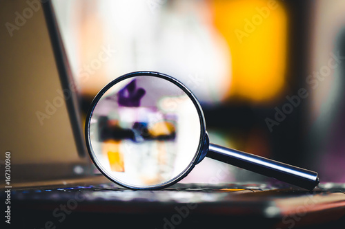 Magnifying glass on laptop keyboard. Internet security concept background.