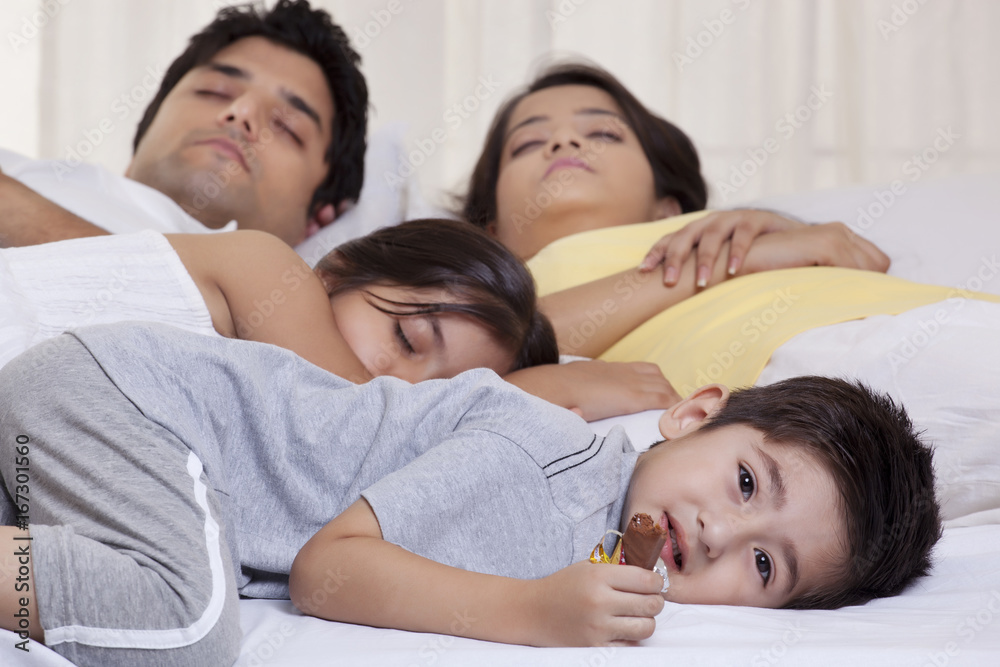 Portrait of boy holding chocolate while his family sleeping in the background Portrait of boy holding chocolate while his family sleeping in the background