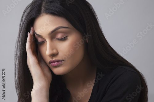 Young Indian female suffering from headache over colored background 