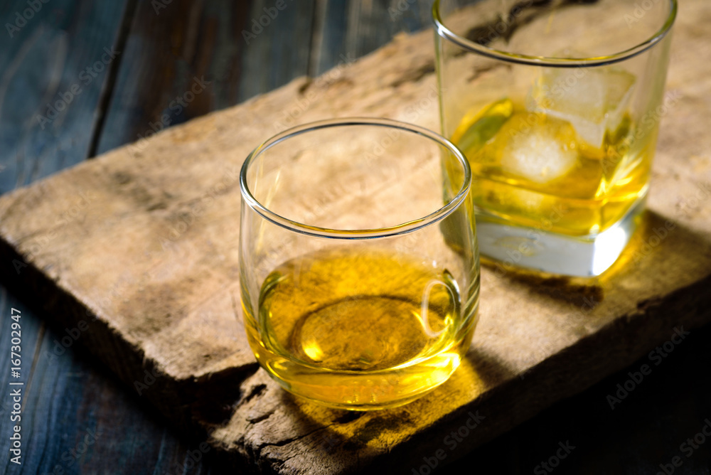 Two glasses of whiskey with ice placed on wooden planks in vintage style. Two glasses of whiskey with ice placed on wooden planks in vintage style.