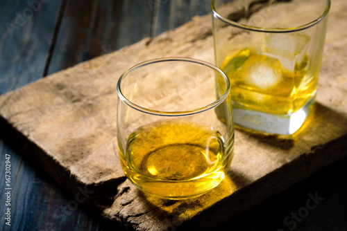 Two glasses of whiskey with ice placed on wooden planks in vintage style.