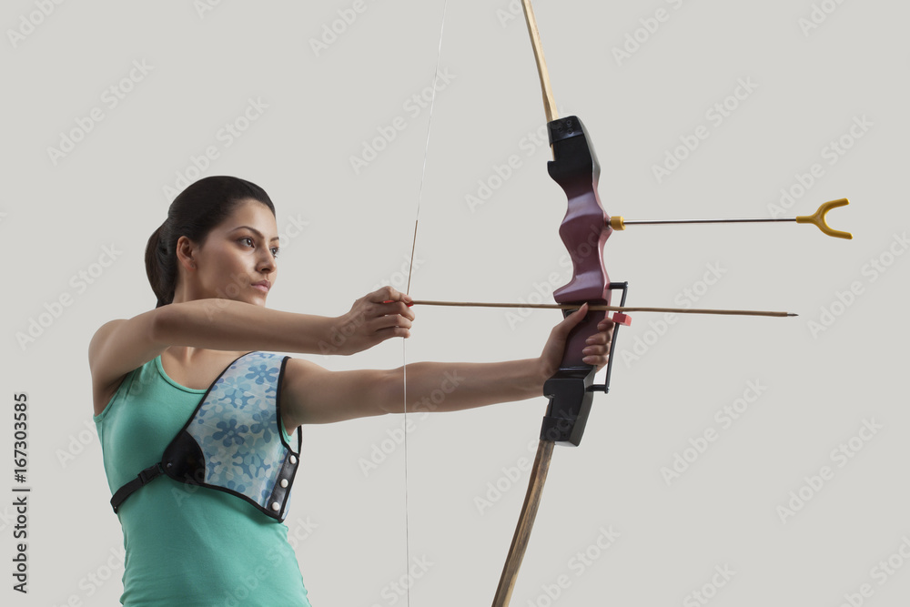 Young female archer with bow and arrow against gray background Young female archer with bow and arrow against gray background