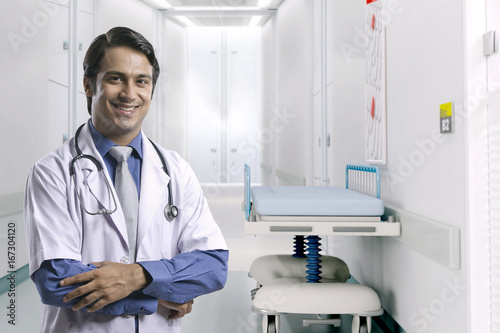 Portrait of smiling male doctor standing arms crossed in hospital corridor
