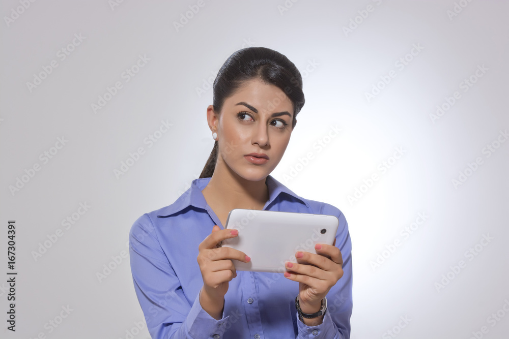 Thoughtful businesswoman holding digital tablet over gray background Thoughtful businesswoman holding digital tablet over gray background