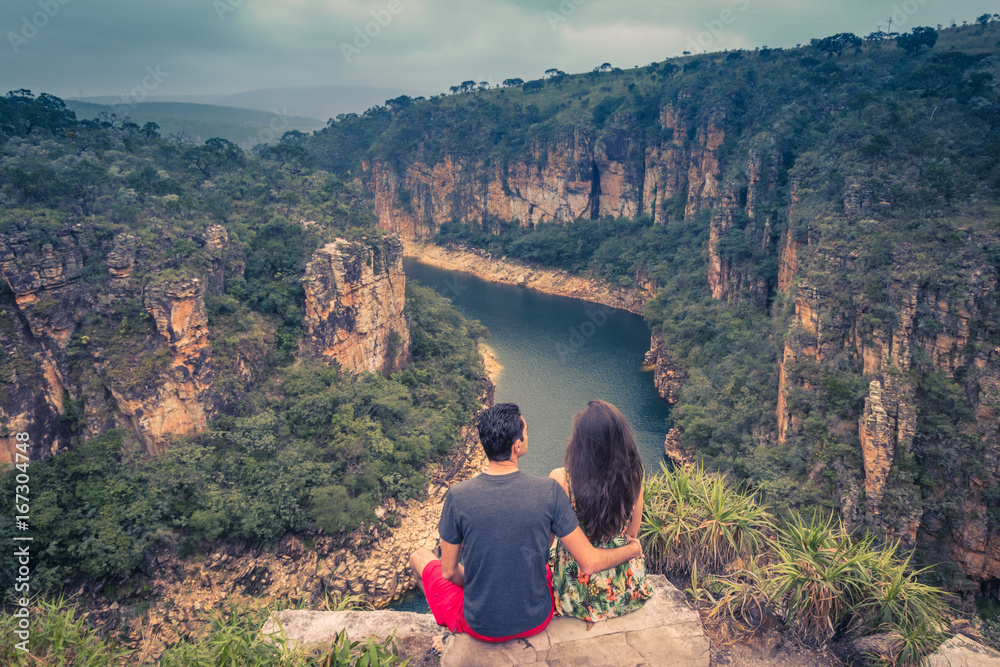 Φωτογραφία Couple on a rock overlooking a canyon with a river on the bottom and rocky walls covered by green trees