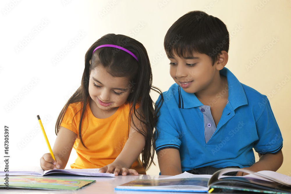 Smiling children studying at table against colored background Smiling children studying at table against colored background