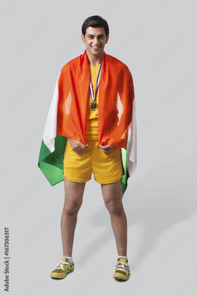 Portrait of young male medalist celebrating victory with Indian flag isolated over gray background Portrait of young male medalist celebrating victory with Indian flag isolated over gray background