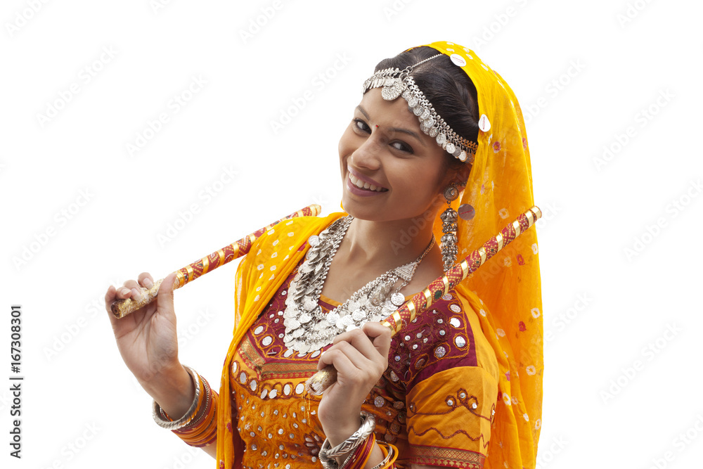 Portrait of happy young woman in traditional wear holding dandiyas ...