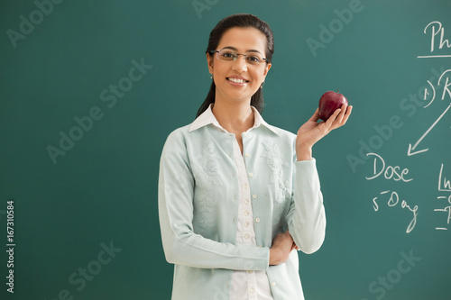 Portrait of young elementary school teacher holding an apple against green board  photo