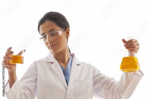 Female scientist holding beaker and flask filled with yellow liquid isolated over white background 
