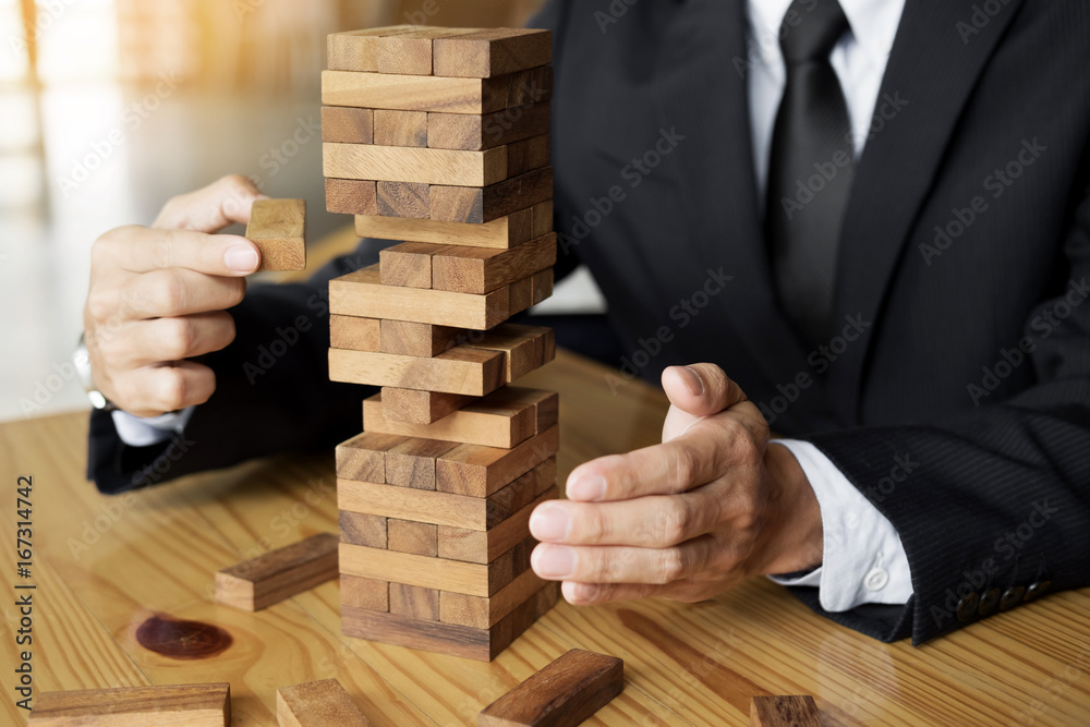 Planning, risk and wealth strategy in business concept, businessman and insurance gambling placing wooden block on a tower Planning, risk and wealth strategy in business concept, businessman and insurance gambling placing wooden block on a tower