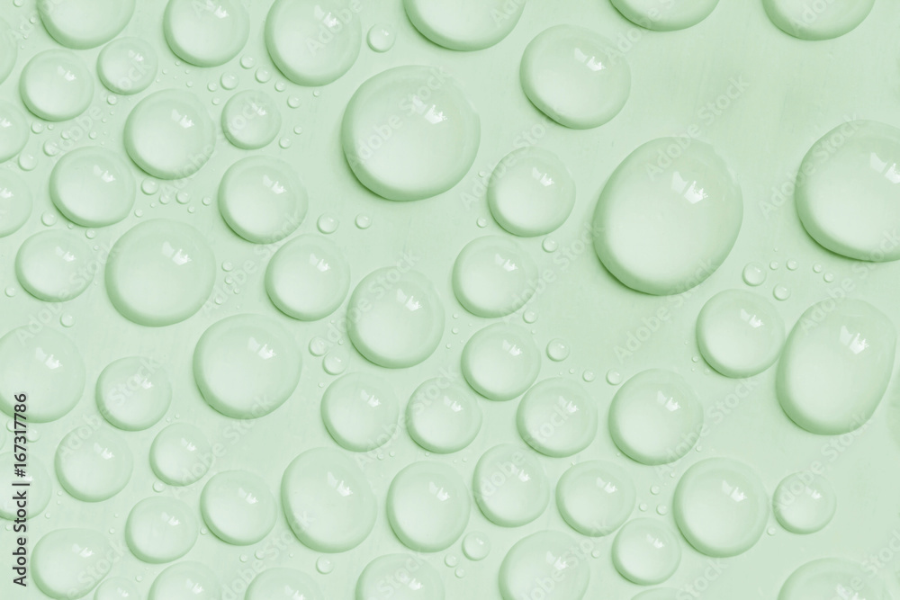 Big and small water drops on light green background. Closeup.